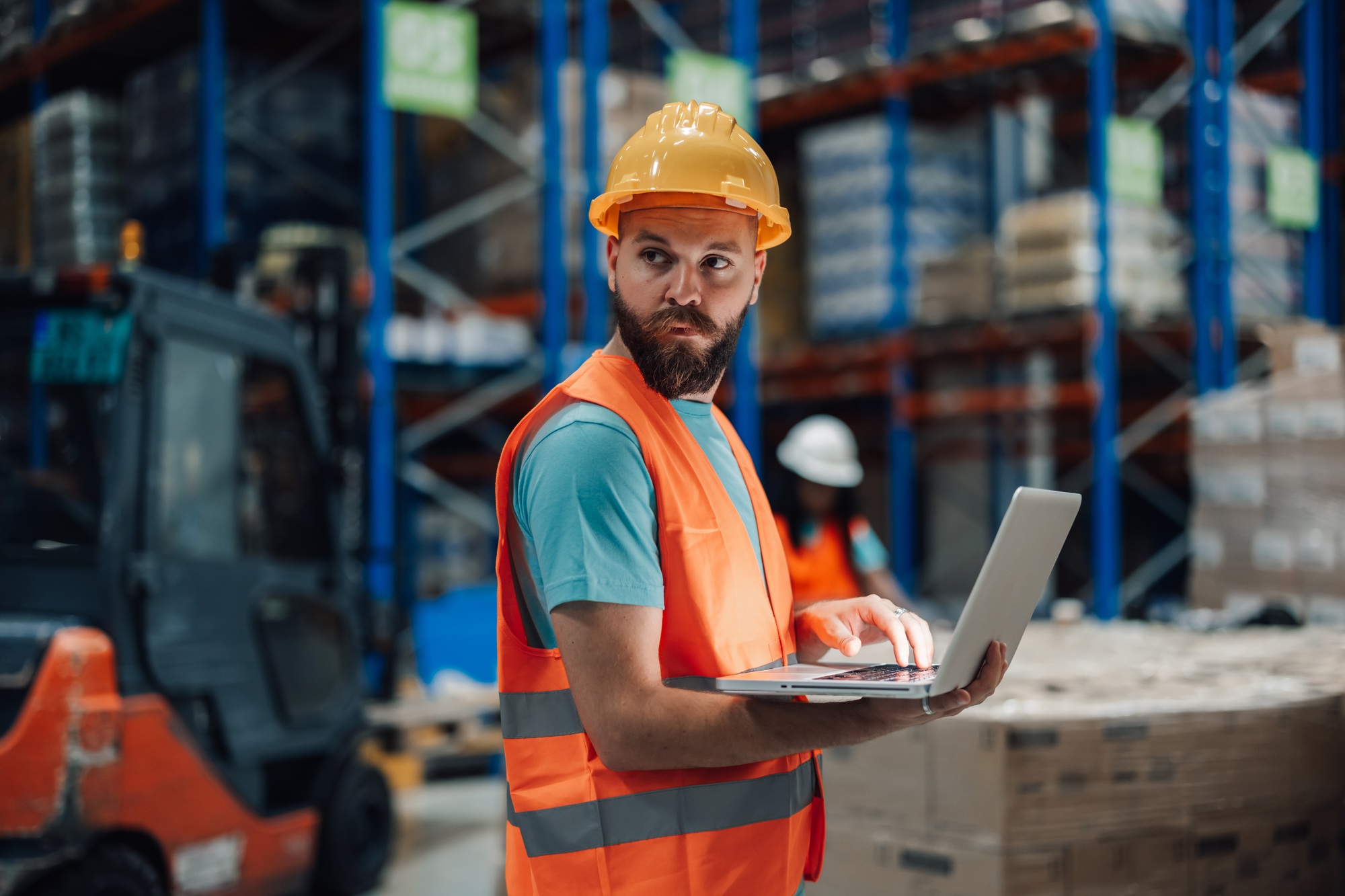 Warehouse worker using laptop and checking inventory in distribution center